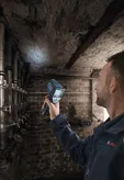 人が地下室の湿った天井を温度検出器でスキャンしています。