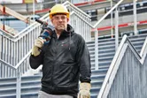 安全装備と加熱パーカーを着用した人が電動工具を持って階段に立っています。