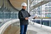 安全装備と加熱ジャケットを着用した人が建設現場で設計図を確認しています。