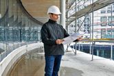 安全装備と加熱ジャケットを着用した人が建設現場で設計図を確認しています。
