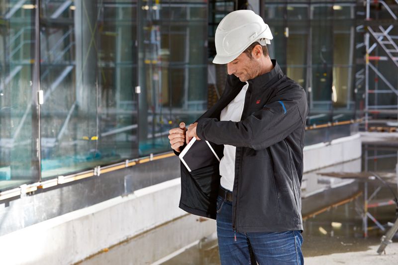 建設現場で安全装備を身に着けた人が加熱ジャケットを調整している。.