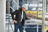 安全装備と加熱ジャケットを着用した人が建設現場でタブレットを検査しています。