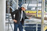 安全装備と加熱ジャケットを着用した人が建設現場でタブレットを検査しています。