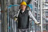 安全装備と加熱ベストを着用した人が建設現場で金属の梁を運んでいます。