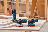 大工の作業場にある木製の作業台には、3 台の電動サンダーが置かれています。.