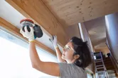 安全装備を身に着けた人がサンダーを使って屋内で木の梁を滑らかにしています。