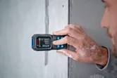 レーザー測定器で壁までの距離を測る人。手についたペイントが見える。