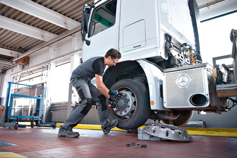 安全装備を身に着けた人がインパクトレンチを使用してトラックの車輪のボルトを締めています。.