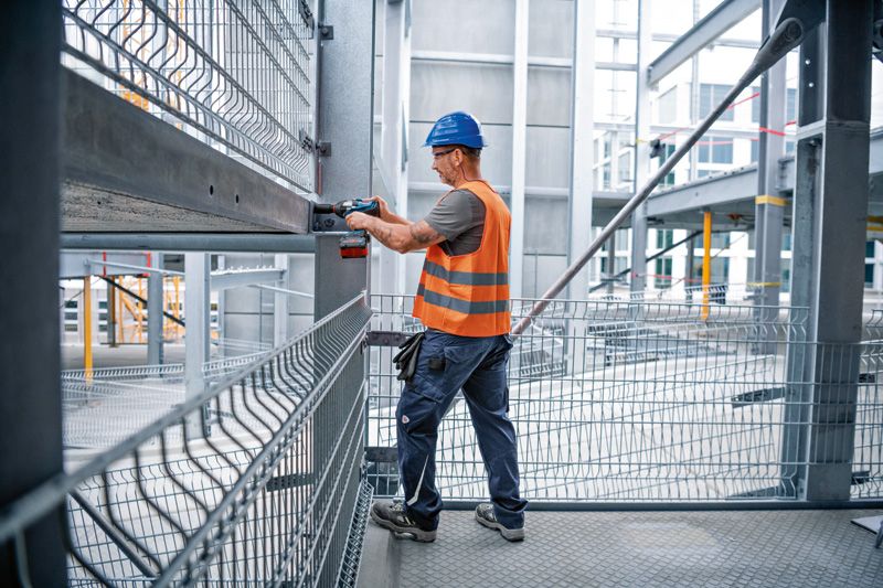 安全装置を装着した人が鉄骨の梁にコードレスインパクトレンチを使用しています。.
