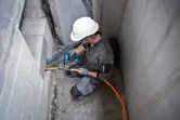 安全装置を装着した人がコードレスヒートガンを使用してオレンジ色のケーブルを作業しています。.
