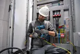安全装置を装着した人が電気配線にコードレスヒートガンを使用しています。.