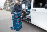 安全装備を身に着けた人が、作業車の横にある台車に積み重ねた工具箱を積み込んでいます。
