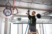 安全装置を装着した人が、はしごの上で FlexiClick アダプターを頭上にしてドリルを使用しています。