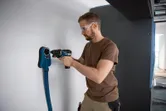 安全装置を装着した人が、集塵機能付き FlexiClick アダプターを使用して壁に穴を開けます。