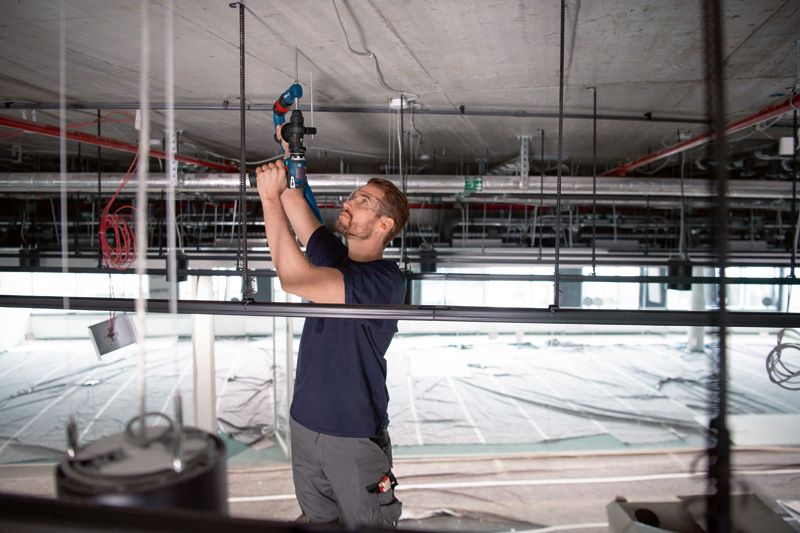 安全装置を装着した人が、FlexiClick アダプター付きのドリルを使用して天井に穴を開けています。