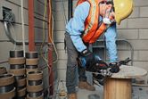安全装備を身に着けた人が建設現場で手持ちののこぎりを使って木材を切っています。