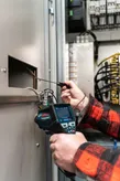 人が温度検出器を使用して電気キャビネット内の配線を確認します。