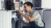 コードレスドライバーを使って洗濯機を修理する人。