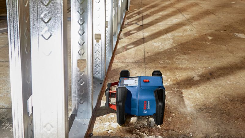 建設現場の床にある金属製の壁フレームの横にガイドラインを投影するレーザーレベルツール。.