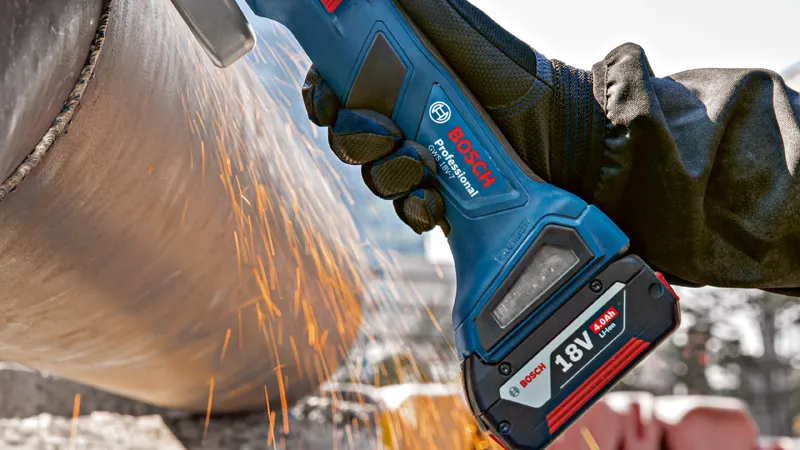 安全装置を装着した人がコードレスアングルグラインダーで金属パイプを研磨しています。.