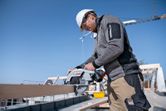 安全装備を身に着けた人が建設現場でコードレス丸鋸を使って木材を切っています。