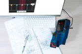 電子検出器が、コンピューターのキーボードの近くの机の上にある技術設計図をスキャンしている。