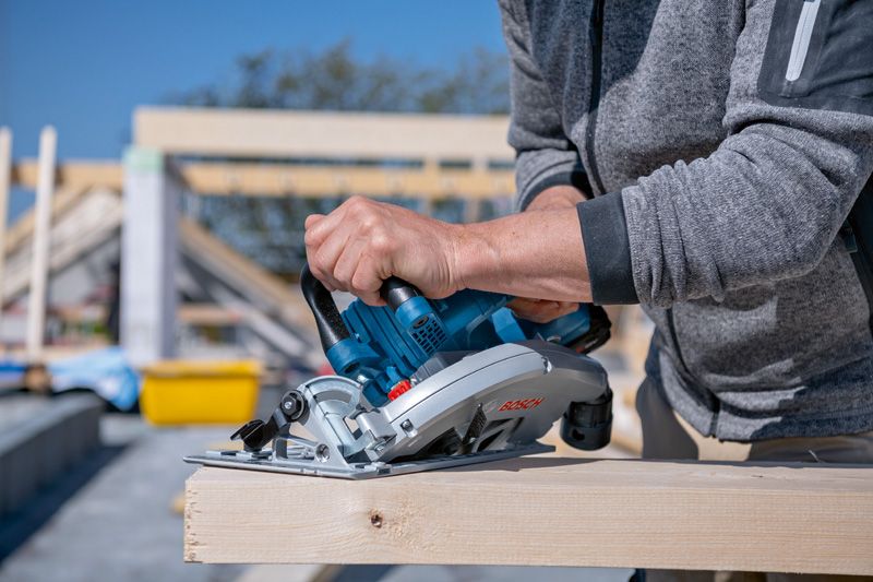 コードレス丸鋸を使用して屋外で木の梁を切る人。.