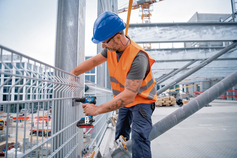 安全装置を装着した人がコードレスインパクトレンチを使用して金属製のフェンスを固定しています。.