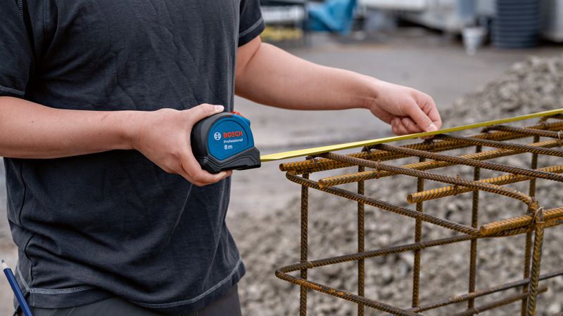 8m オートロックテープ M 人が巻尺を使用して金属鉄筋構造の幅を確認します。.