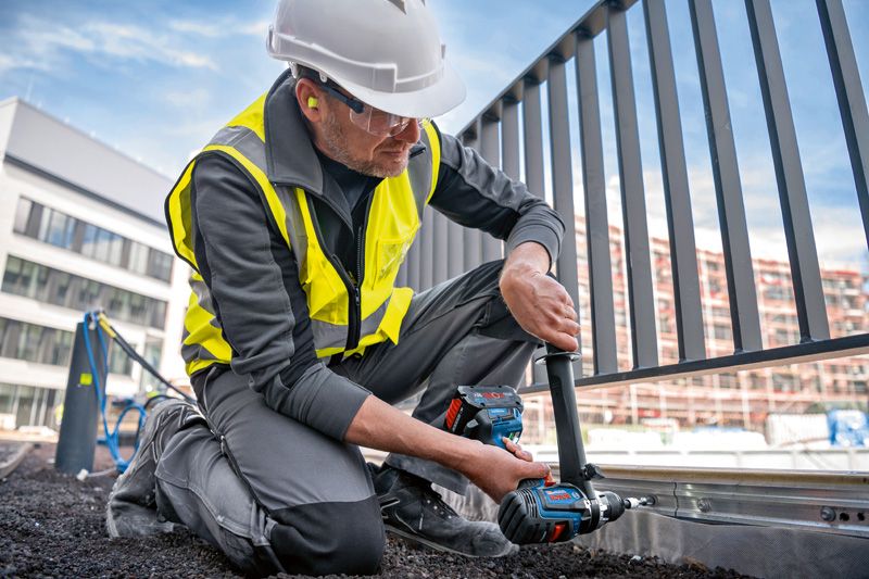 安全装置を装着した人が金属製のフェンス フレームでコードレス コンビ ドリルを使用しています。.