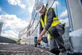 安全装置を装着した人が建設現場でコードレスドリルドライバーを使用しています。.