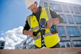 安全装置を装着した人が建設現場でコードレスドリルを使用して木材に穴を開けています。