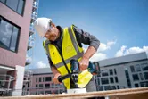 安全装備を身に着けた人が建設現場で木材に穴を開けています。
