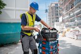 安全装備を身に着けた人が建設現場で工具箱を整理しています。.