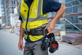 安全装備を着用した人が建設現場で工具ベルトを調整しています。.