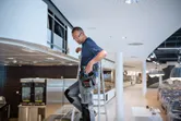 安全装備を身に着けた人がはしごの上に立ち、換気システムを設置しています。.