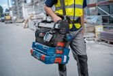 安全装備を身に着けた人が、建設現場で積み重ねられた工具箱とデジタル角度測定器を運んでいます。