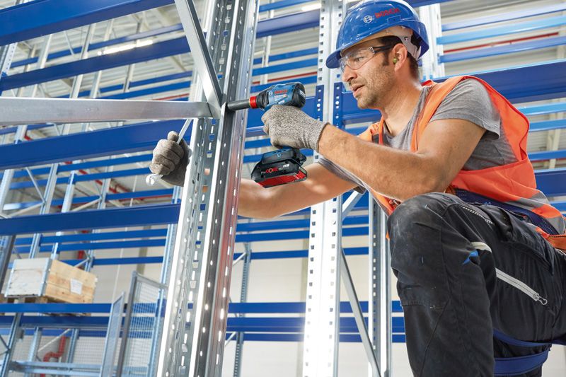 安全装置を装着した人がコードレスドリルを使用して金属製の棚を組み立てています。.