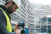 安全装備を装着した人が建設現場でレーザー測定器を操作しています。