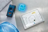 設計図の横にレーザー測定器があり、タブレットにはデジタルのフロアプランが表示されています。