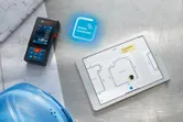 建築図面の横にあるレーザー測定器、間取り図を表示するタブレット、安全ヘルメット。
