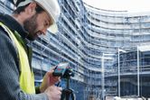 建設現場では安全装備を装着した人がレーザー測定器を使用しています。