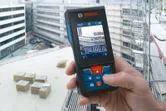 足場と積み重ねられた木箱のある建設現場で、人がレーザー測定器を操作しています。