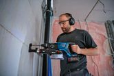 安全装置を装着した人が、集塵装置が組み込まれた工具を使用して壁に穴を開けています。