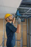 安全装備を身に着けた人が電動工具で金属製の天井枠を固定しています。