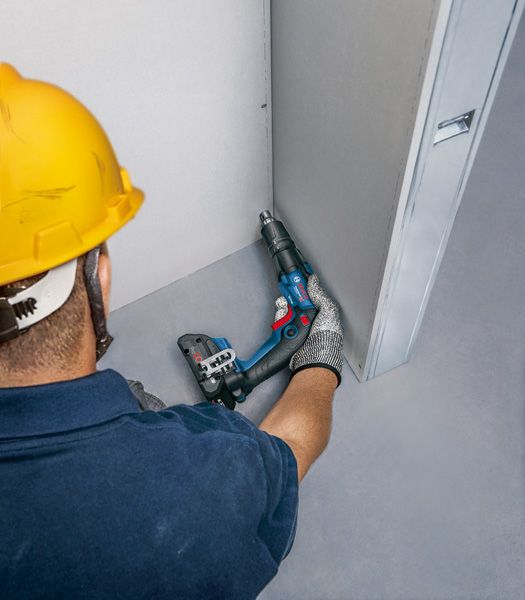 安全装置を装着した人が電動工具で乾式壁にネジを打ち込んでいます。.