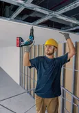 安全装置を装着した人が電動ドライバーを使用して天井パネルを設置します。