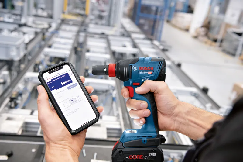 産業現場で、スマートフォンを使ってコードレスドリルを操作する人。.