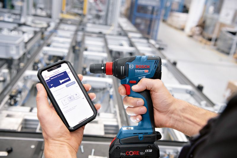 産業現場で、スマートフォンを使ってコードレスドリルを操作する人。.