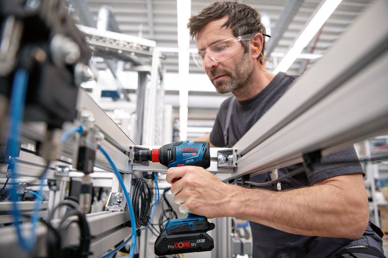 安全装置を装着した人がコードレスドリルを使用して金属フレームを固定しています。.